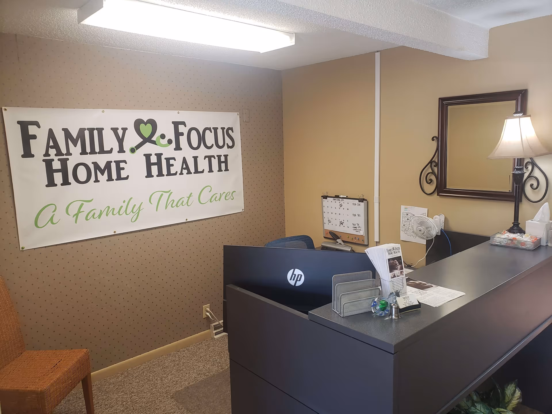 Reception desk with an HP monitor, a wall banner, and a lamp in a clinic-like lobby.