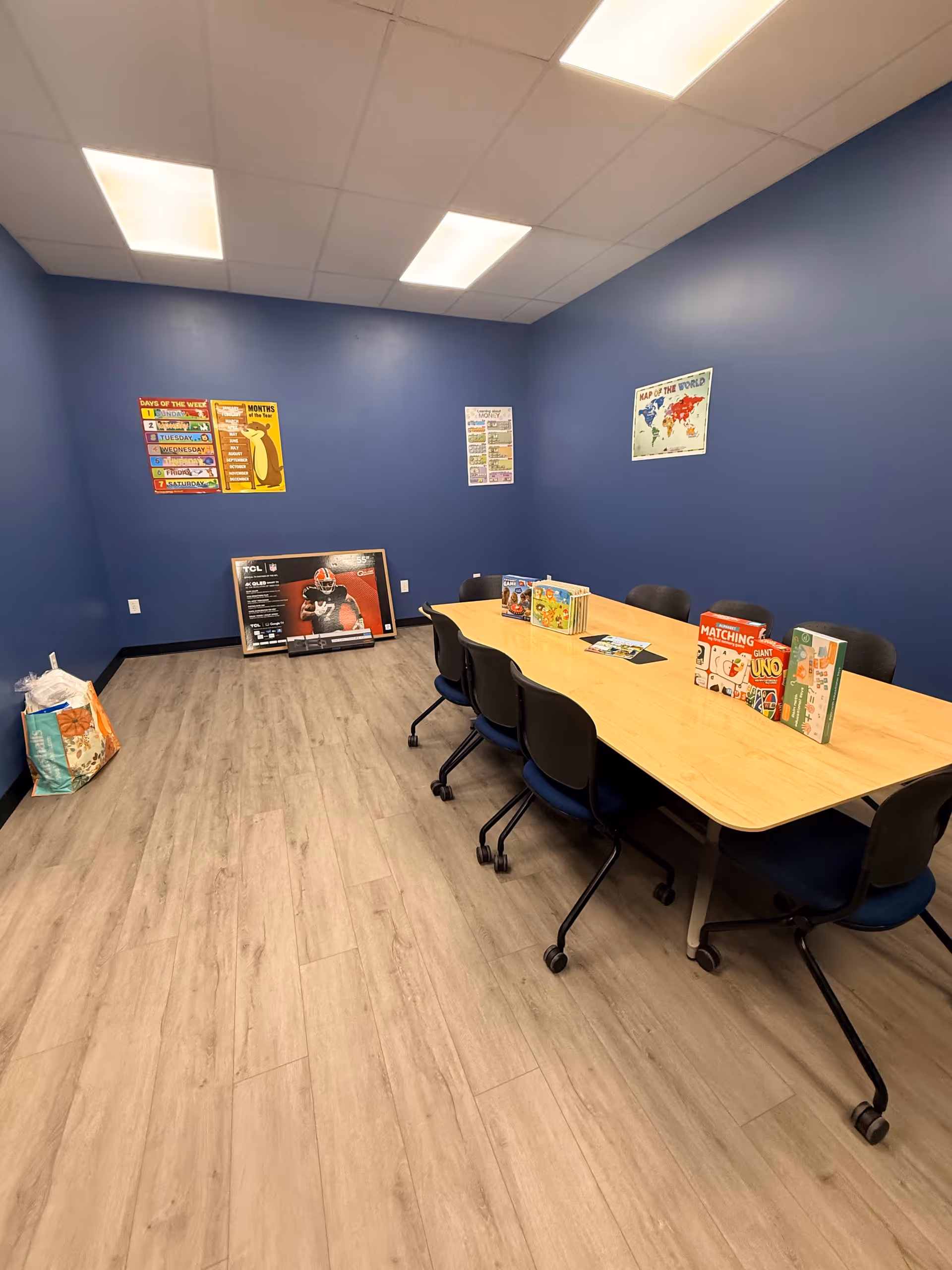 Blue-walled activity room with a long table, chairs, and board games.