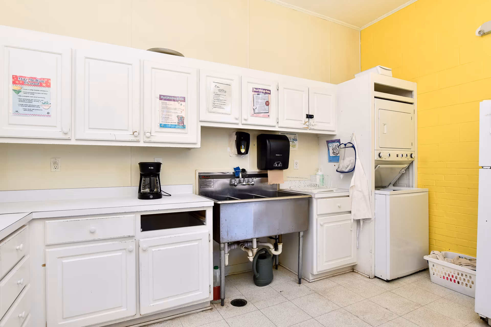 White cabinets, stainless sink, and coffee maker in a bright facility kitchen.