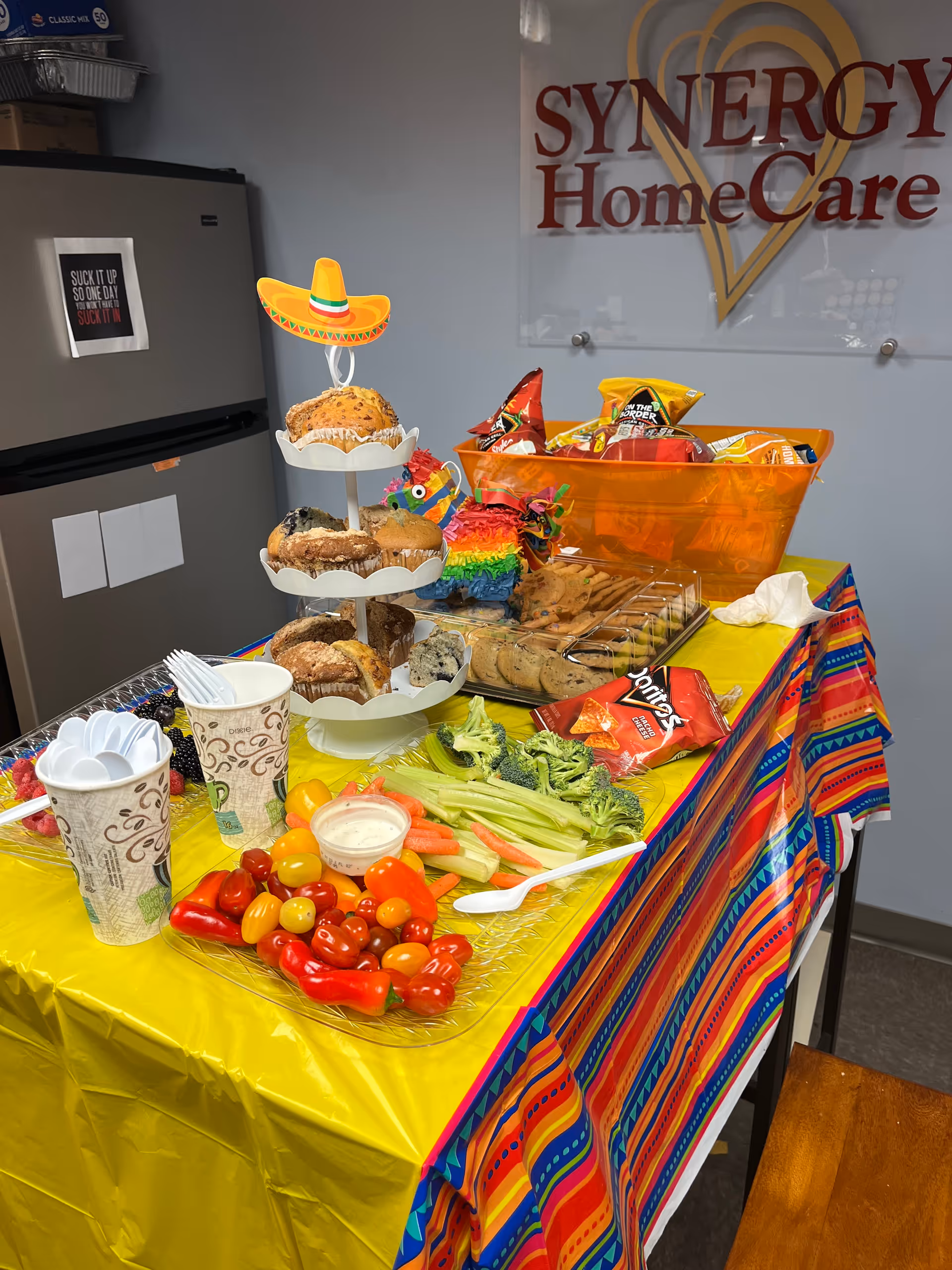 Colorful food table with vegetables, pastries, chips, and drinks at a Synergy HomeCare event.