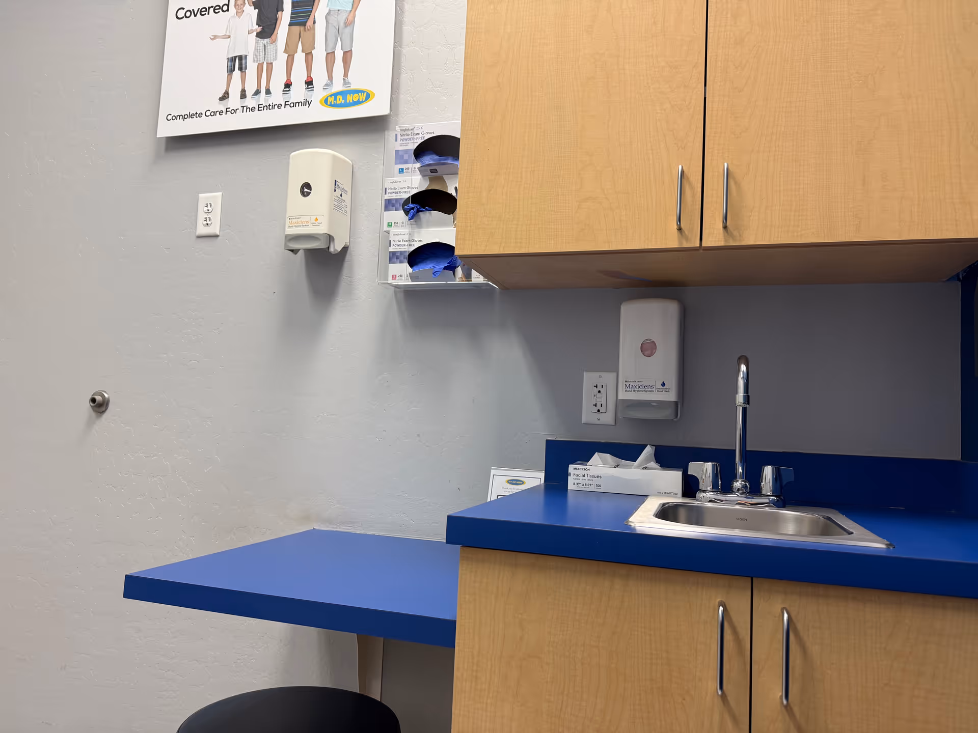 Blue countertop with sink and wooden cabinets in a small clinical kitchen area.
