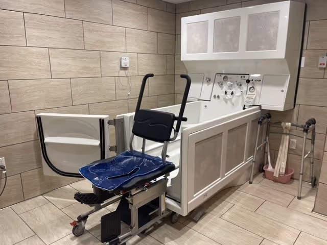 White bath lift chair with blue seat in a tiled senior care bathroom.