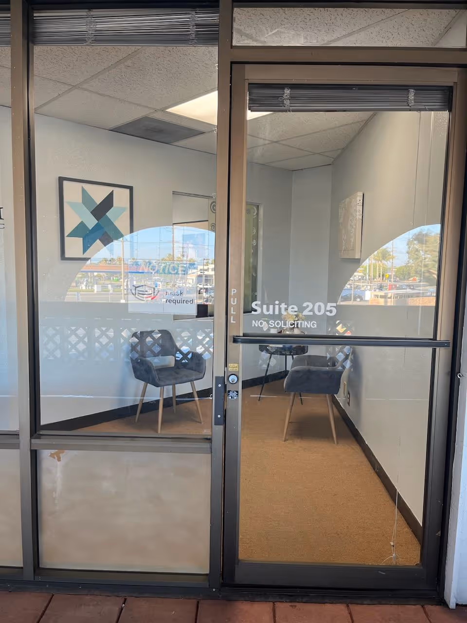 Glass entrance to a facility lobby with two chairs, Suite 205, No Soliciting.