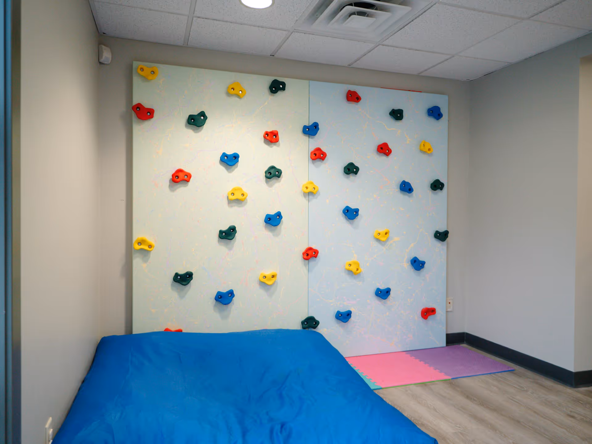 Indoor therapy room featuring a climbing wall with colorful holds and mats.