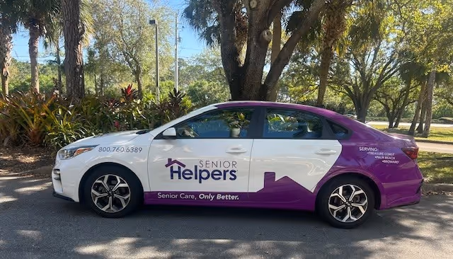 A purple-and-white Senior Helpers branded car parked outdoors.