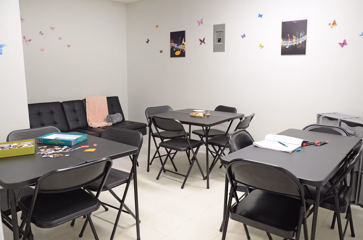 Small, well-lit indoor activity room with black folding tables, chairs, a sofa, and butterfly decals.