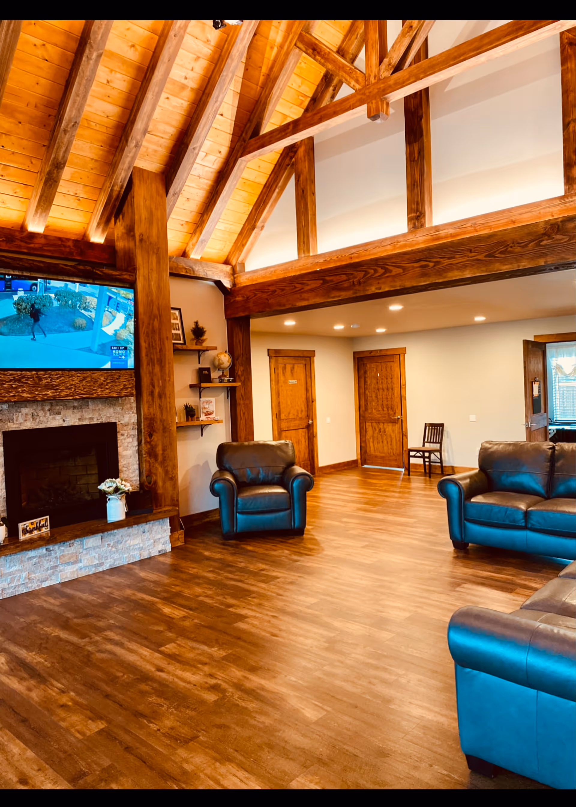 Rustic indoor living room with vaulted wooden beams, leather seating, and a fireplace.