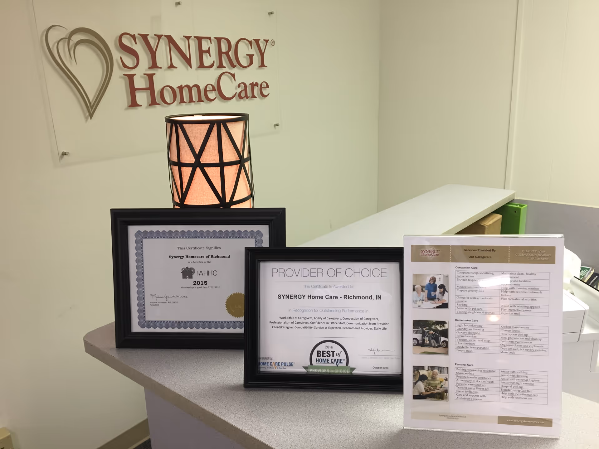 Reception desk with framed certificates and a Synergy HomeCare sign on the wall.