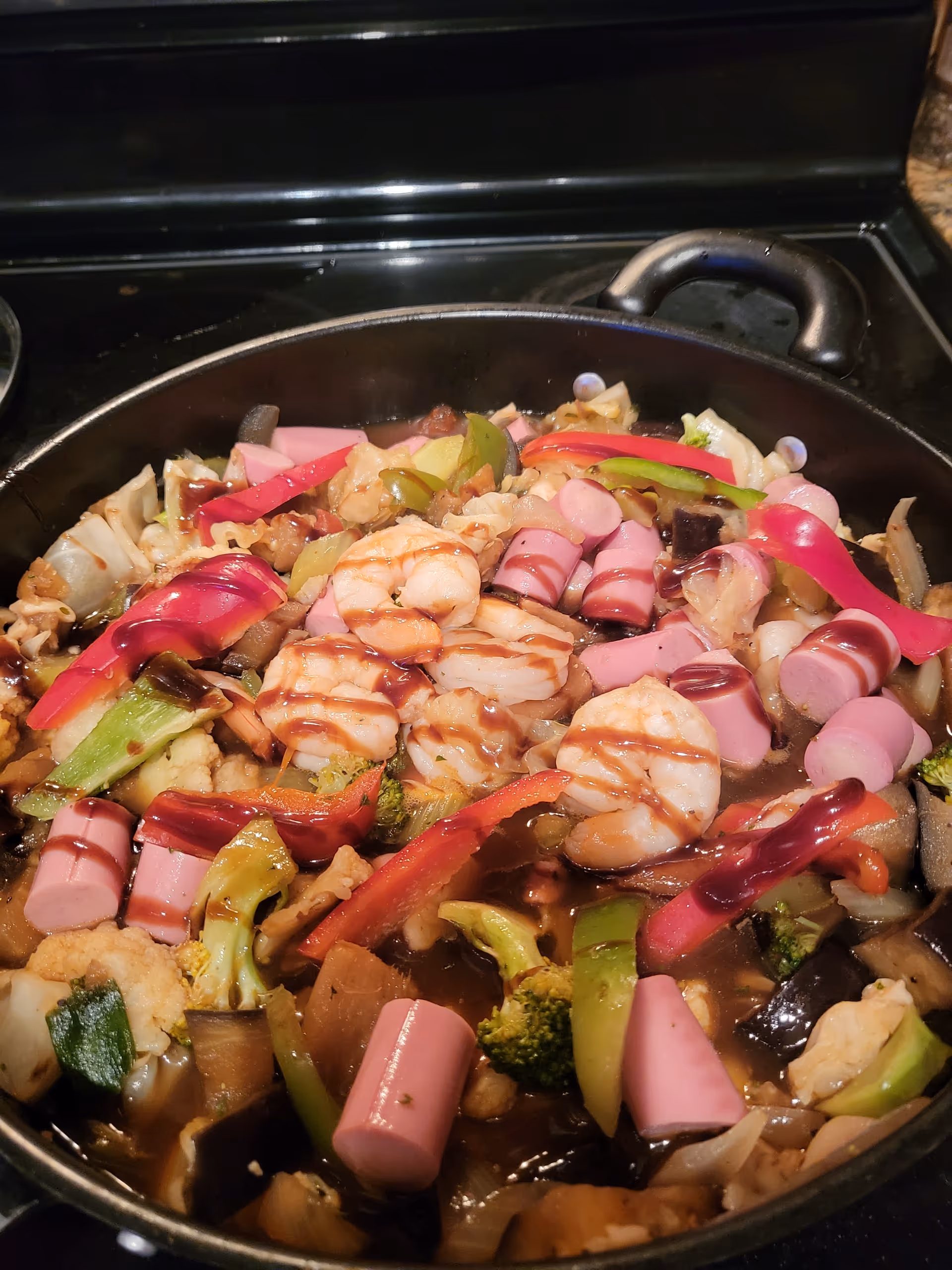 Pan of shrimp, vegetables, and pink sausage cooking on a stove.