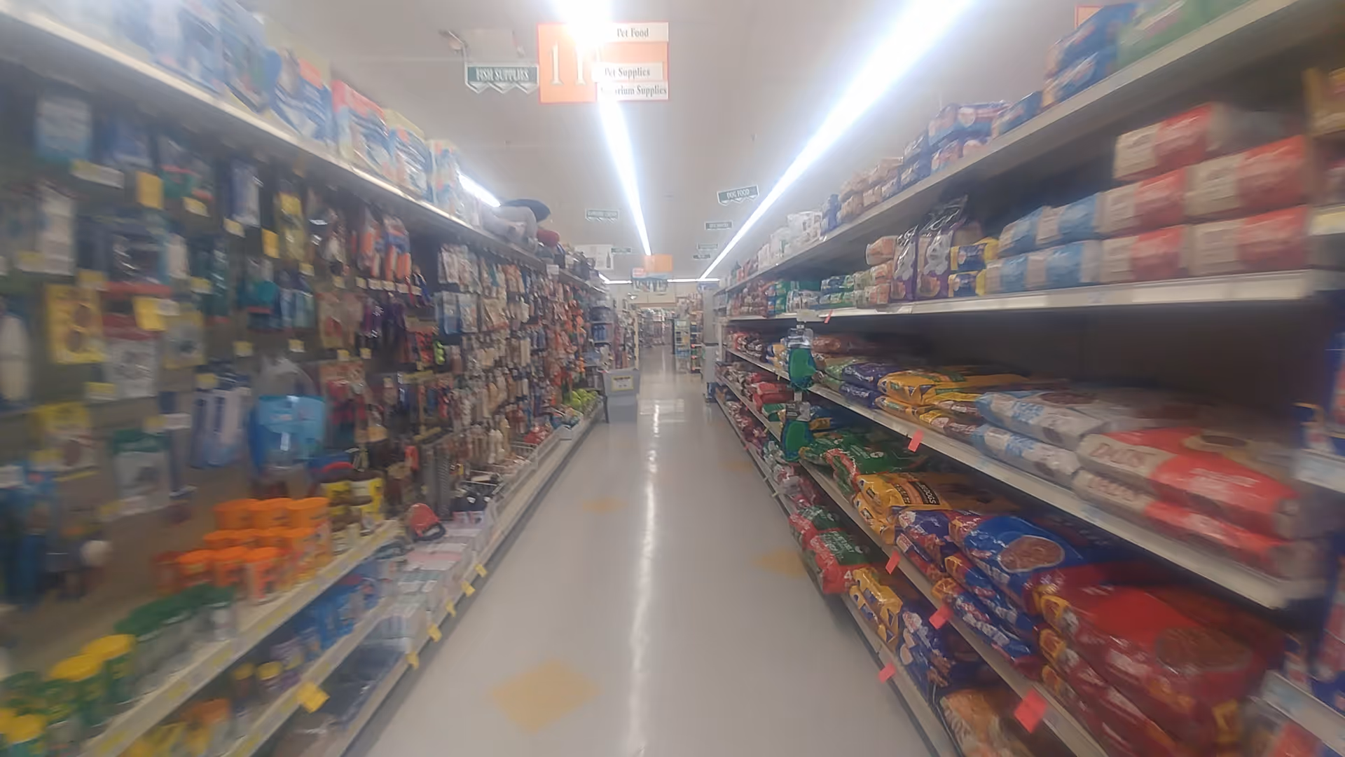 Blurry view of a long pharmacy aisle with shelves stocked on both sides.