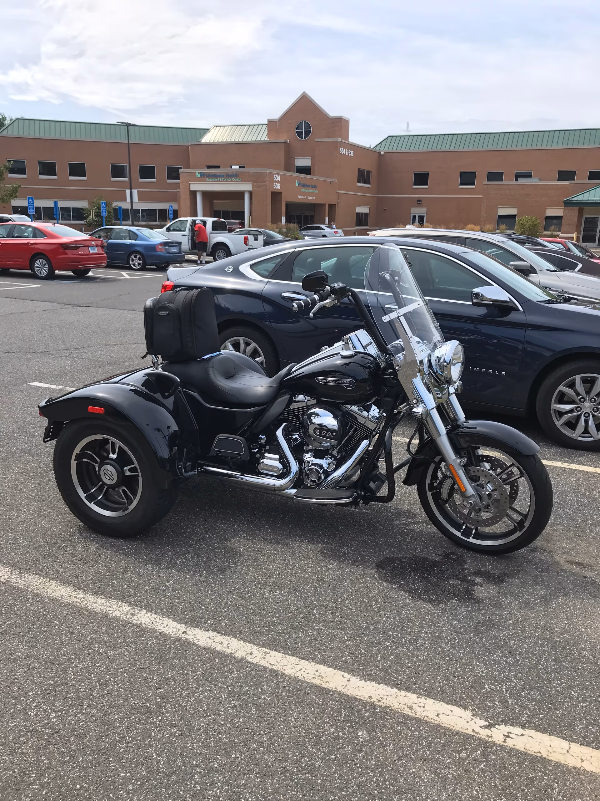 Black motorcycle parked in a lot with a brick medical facility in the background.