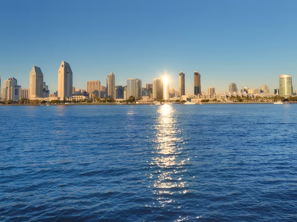 City skyline across a blue harbor with sun reflection on the water.