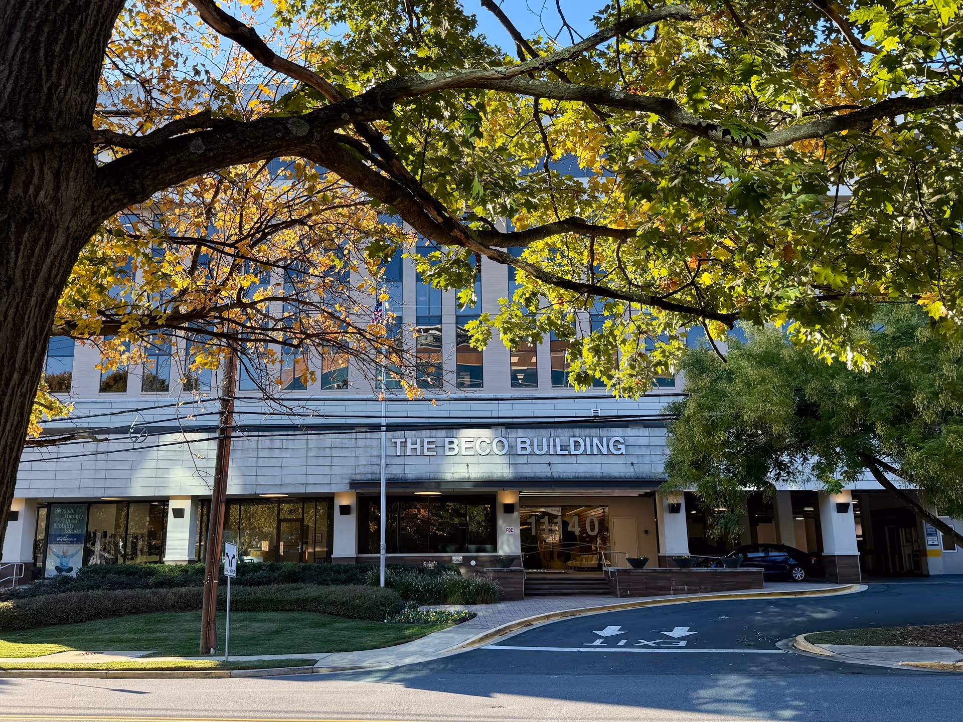 Exterior view of a multi-story building named The BECO Building with trees in front.