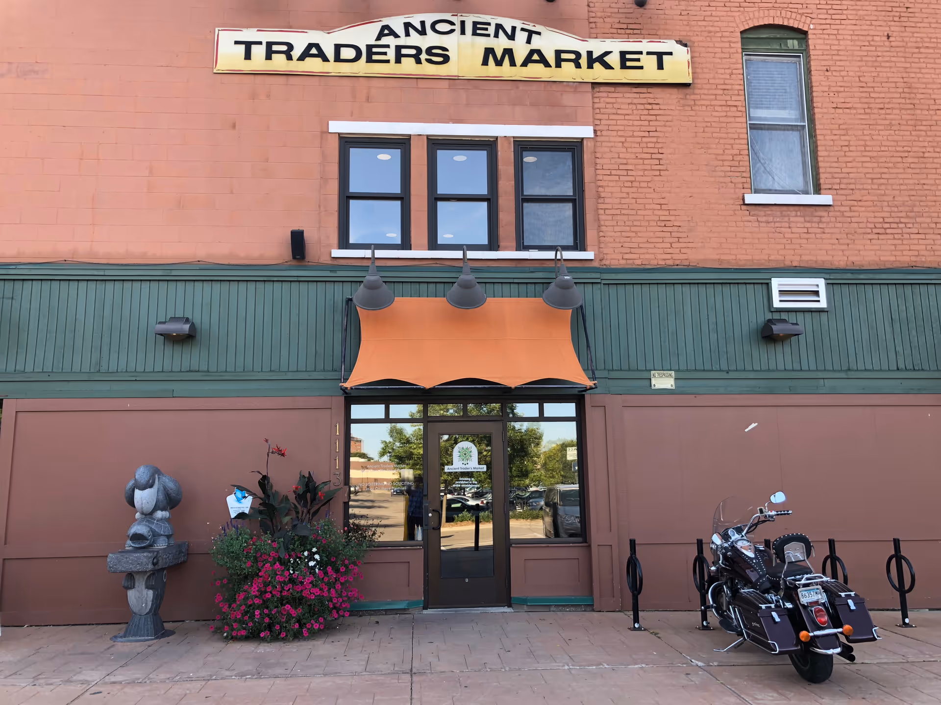 Storefront building with orange awning, glass entrance, flower planters, and a motorcycle outside.