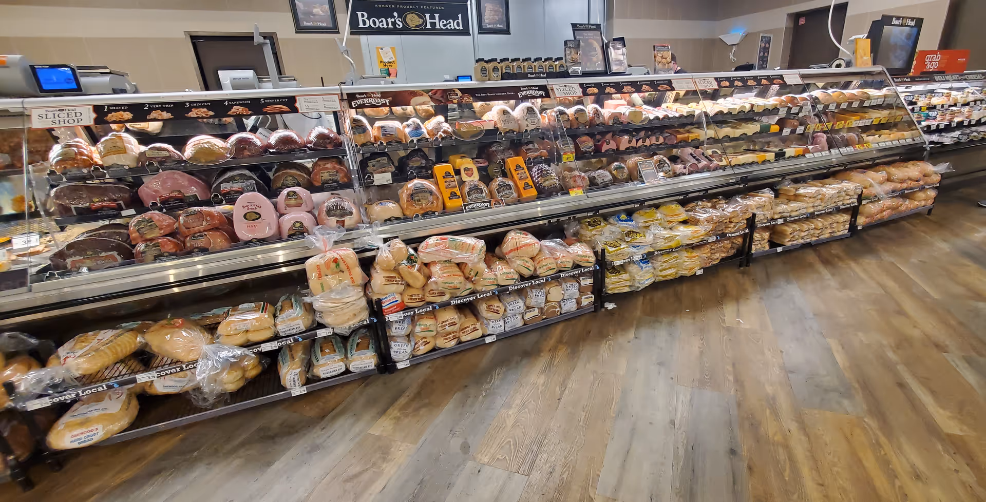 Long refrigerated deli display case with assorted meats and breads in Kroger.