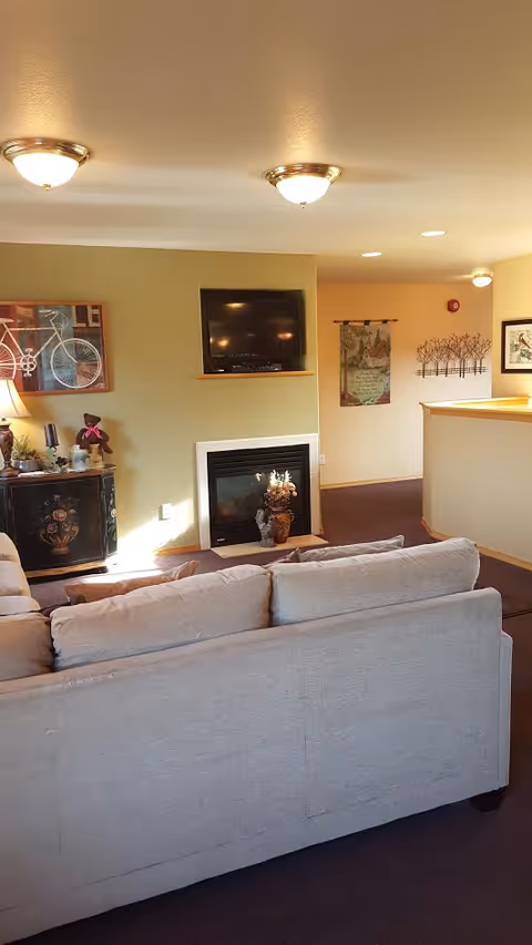 Cozy resident lounge with sofa, fireplace, wall-mounted TV, and decorative art.