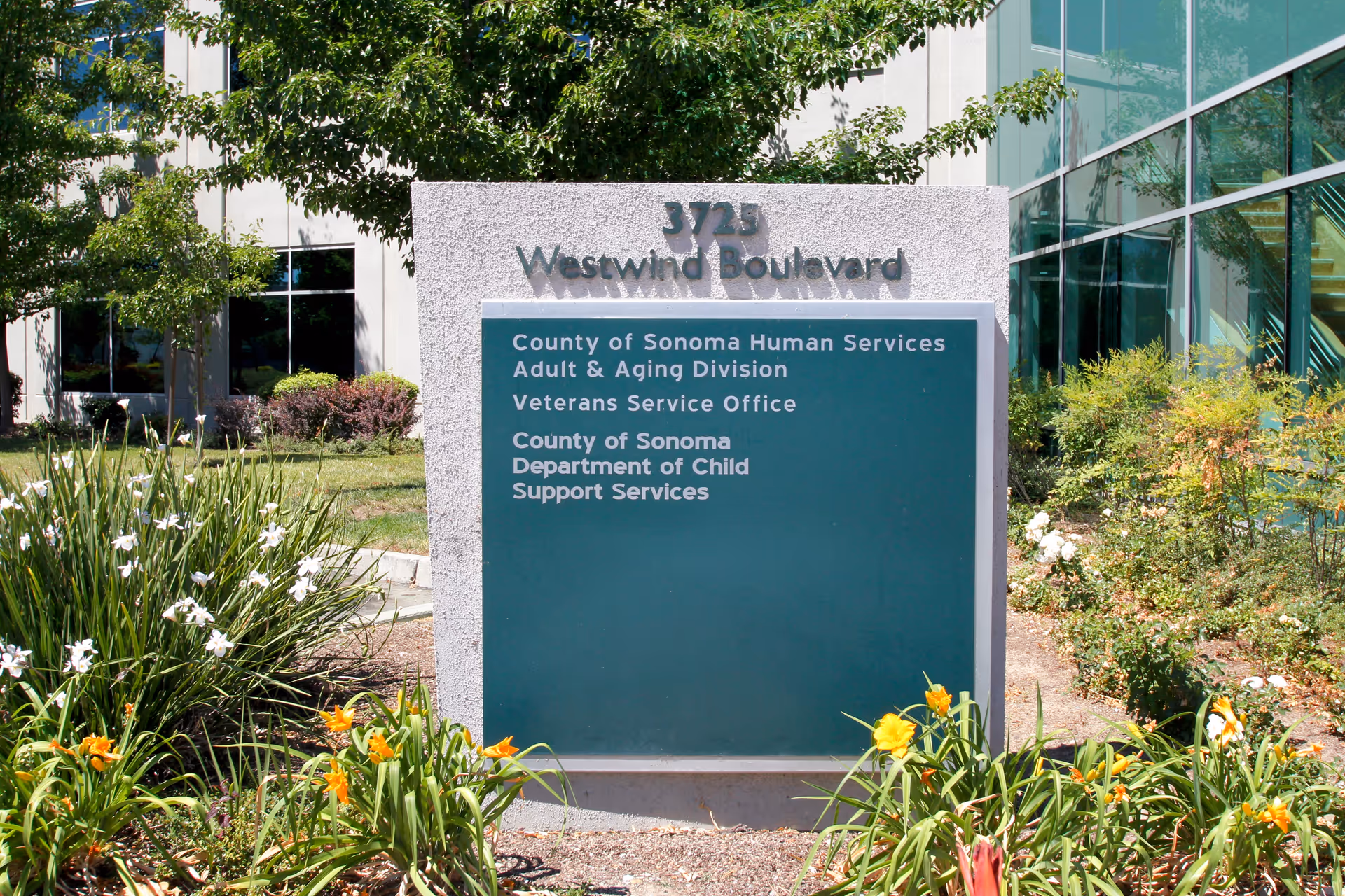 Stone sign reading Westwind Boulevard in front of a glass-building with flowering plants.
