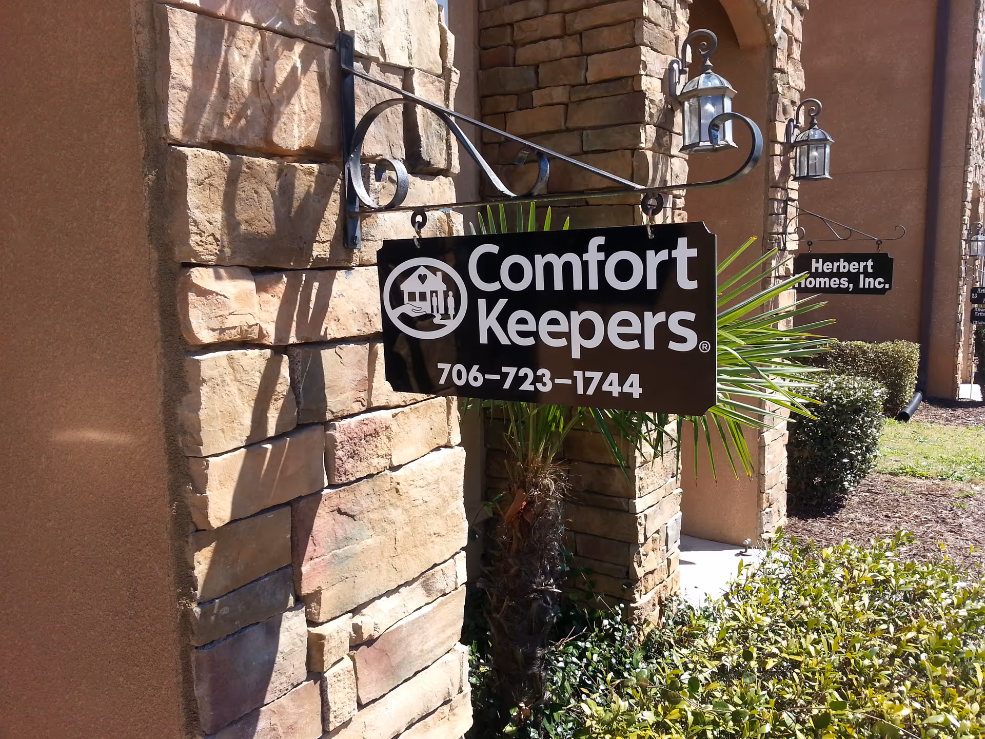 Front exterior sign for Comfort Keepers mounted on a stone wall by the entrance.