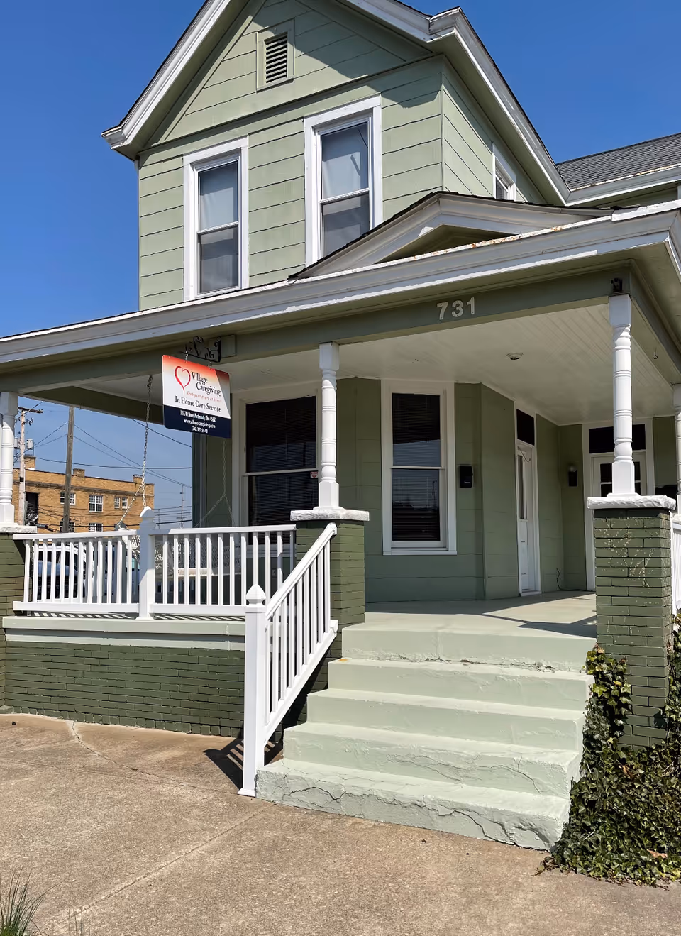 A green two-story building with a covered porch, white railing, and Village Caregiving sign.