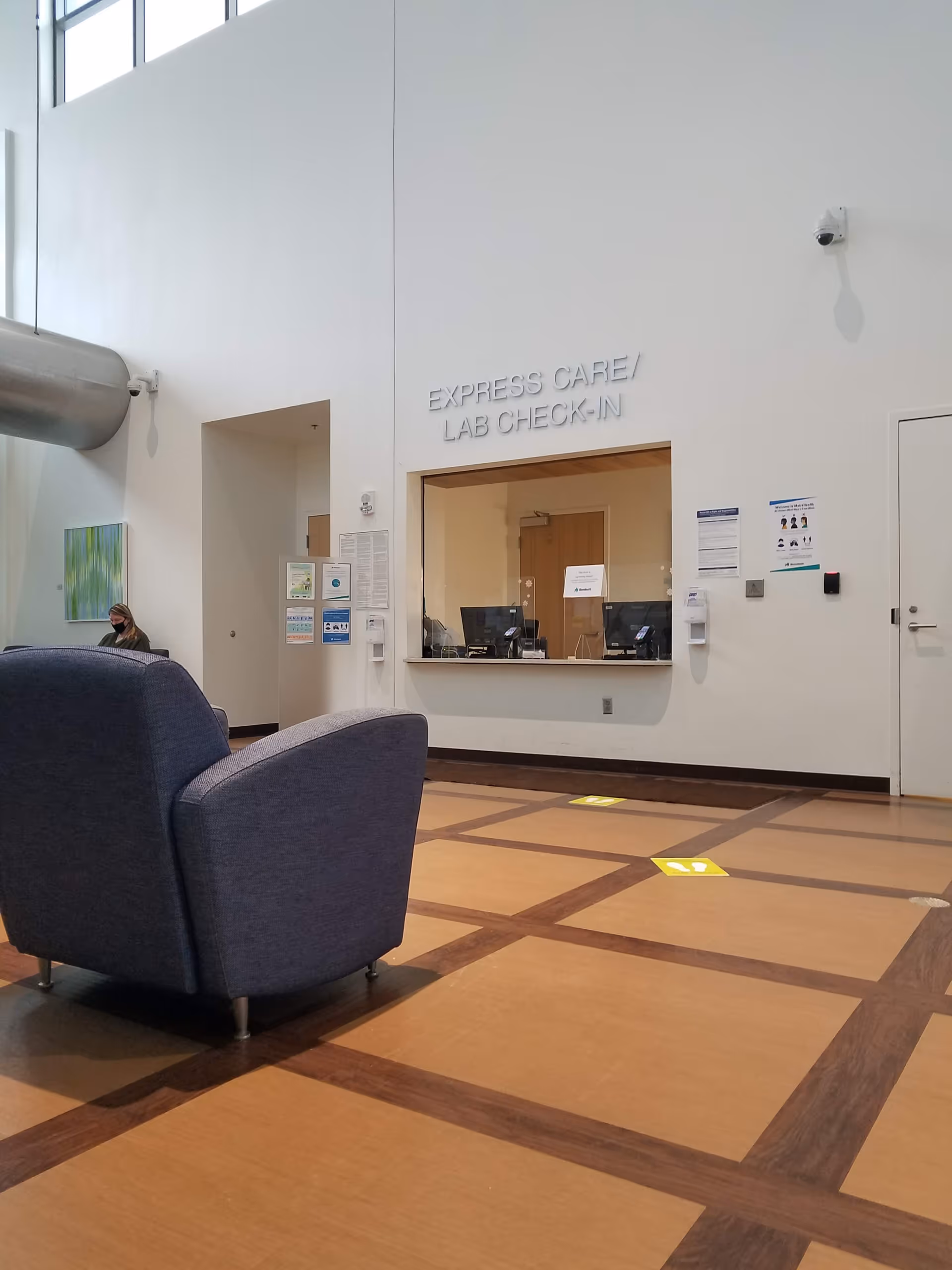 Bright hospital lobby with Express Care/ Lab Check-In window and blue seating.