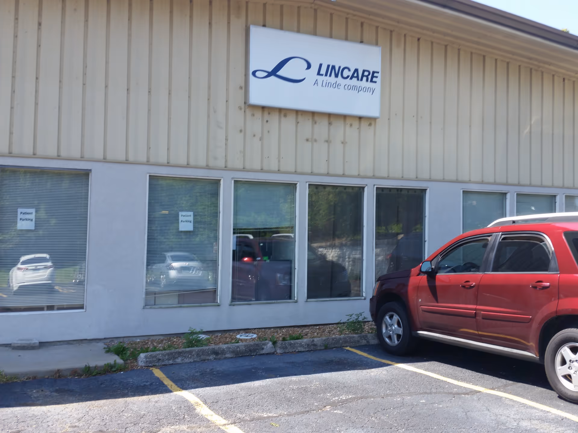 Front exterior of a LINCARE building with large windows and a red SUV parked outside