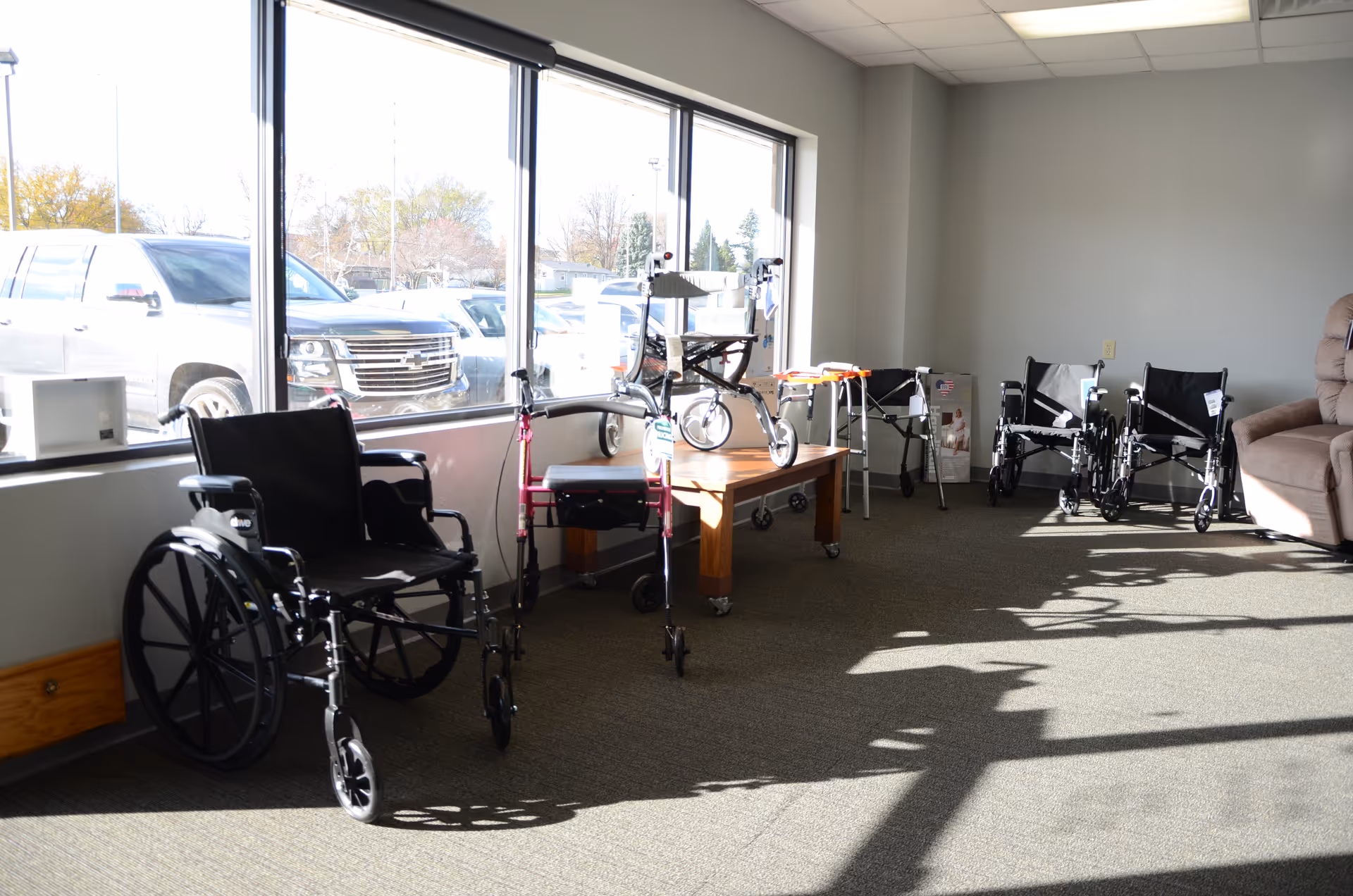 Wheelchairs and walkers line a bright interior lounge near large windows.