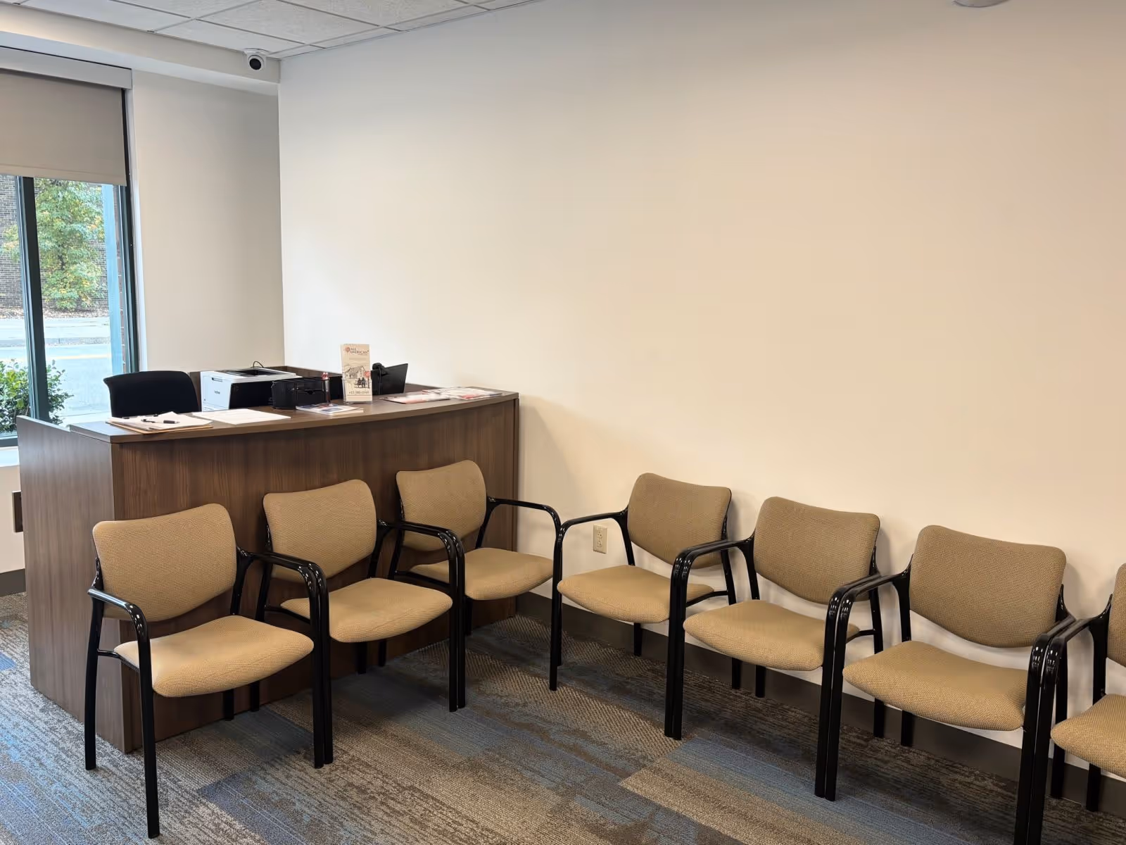 Reception desk with row of beige chairs in a waiting area.