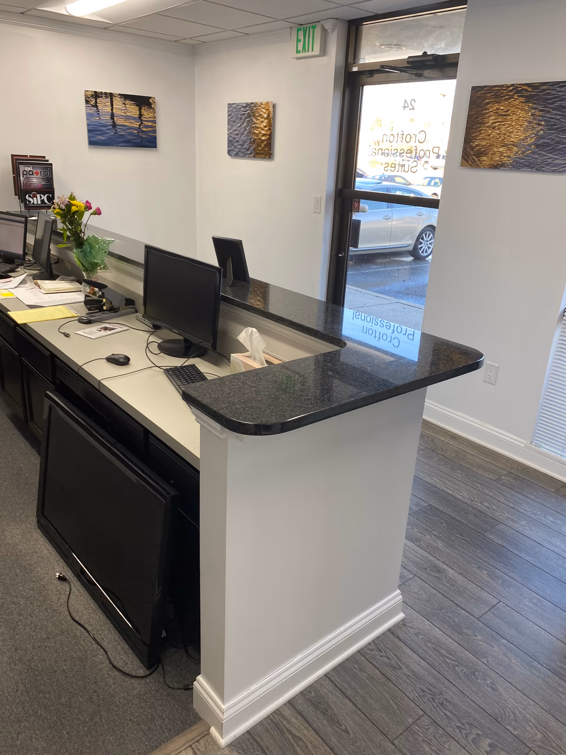 Reception desk with computers, tissue box, flowers, and wall art in a facility lobby.