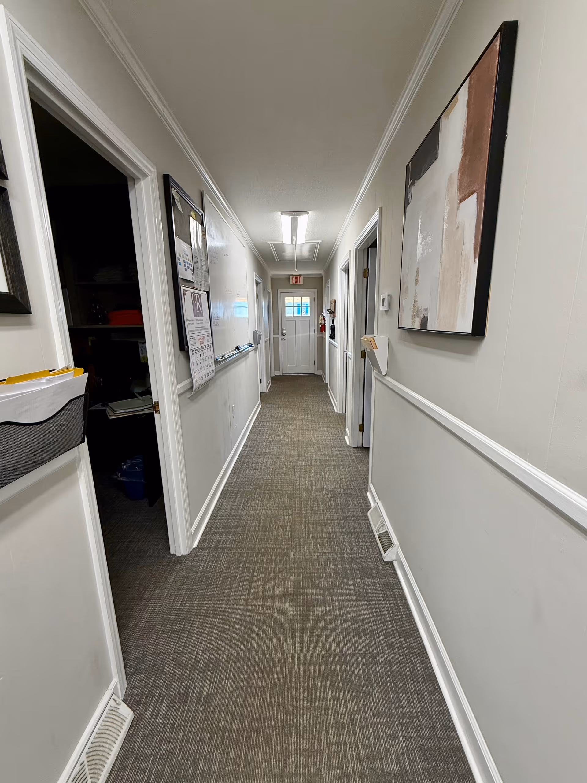 Long carpeted hallway inside a senior care facility with doors, bulletin board, and wall art.