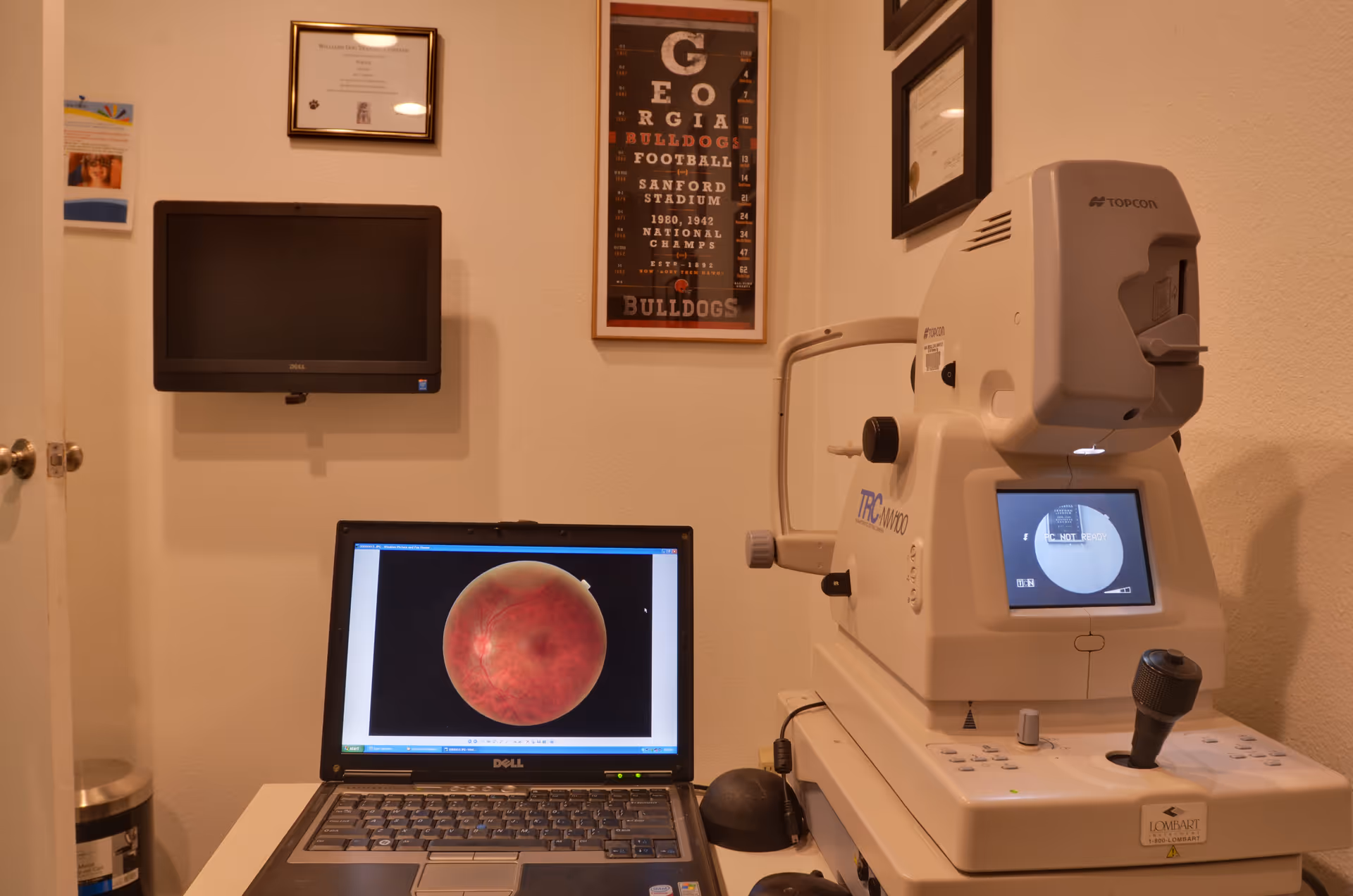 Opulent Eyes Optometry exam room with a laptop displaying a retinal image beside an OCT device.