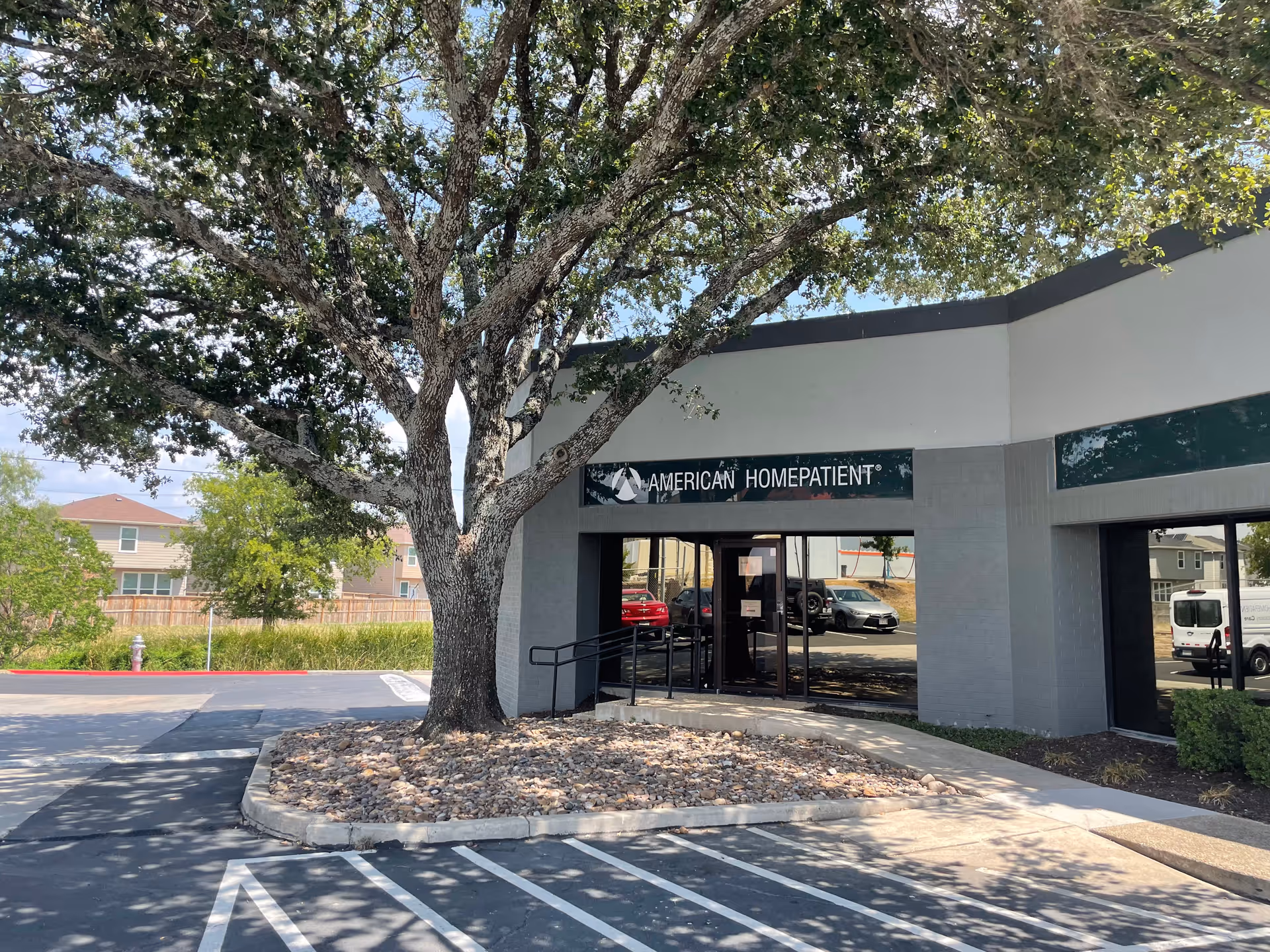 Exterior view of American HomePatient building with glass doors and a large tree.