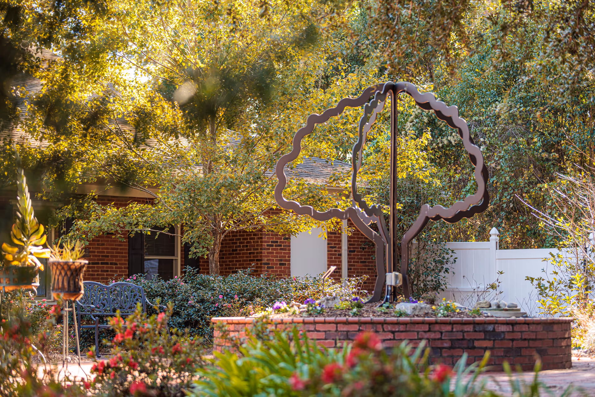 Outdoor courtyard with brick planter, sculpture, trees, and seating at a senior living facility.