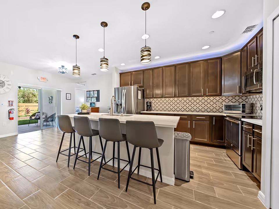 Modern kitchen with dark wood cabinets, island, and bar stools in a senior living facility.