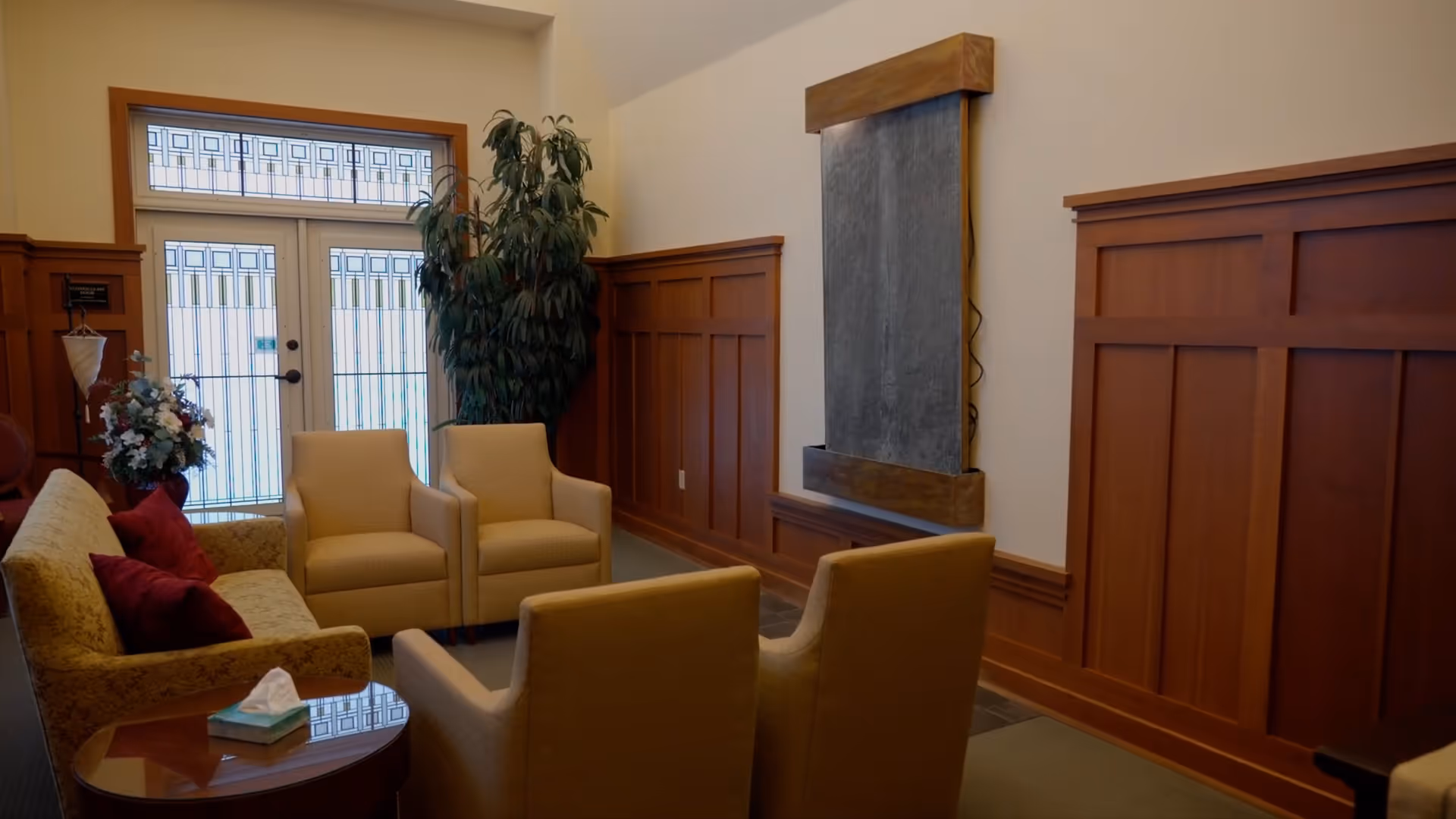 A cozy lounge with beige seating, wood-paneled walls, and a glass door.