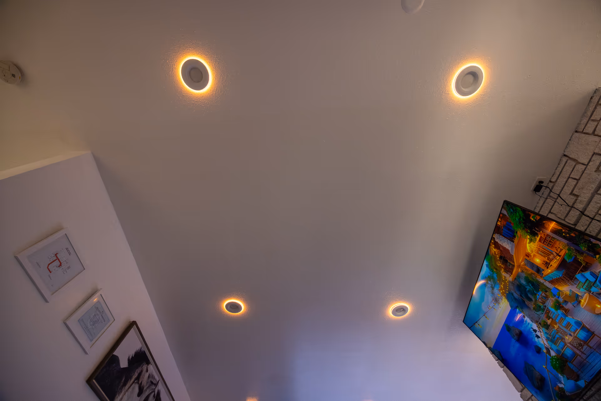 White ceiling with circular recessed lights, TV on wall, framed art.