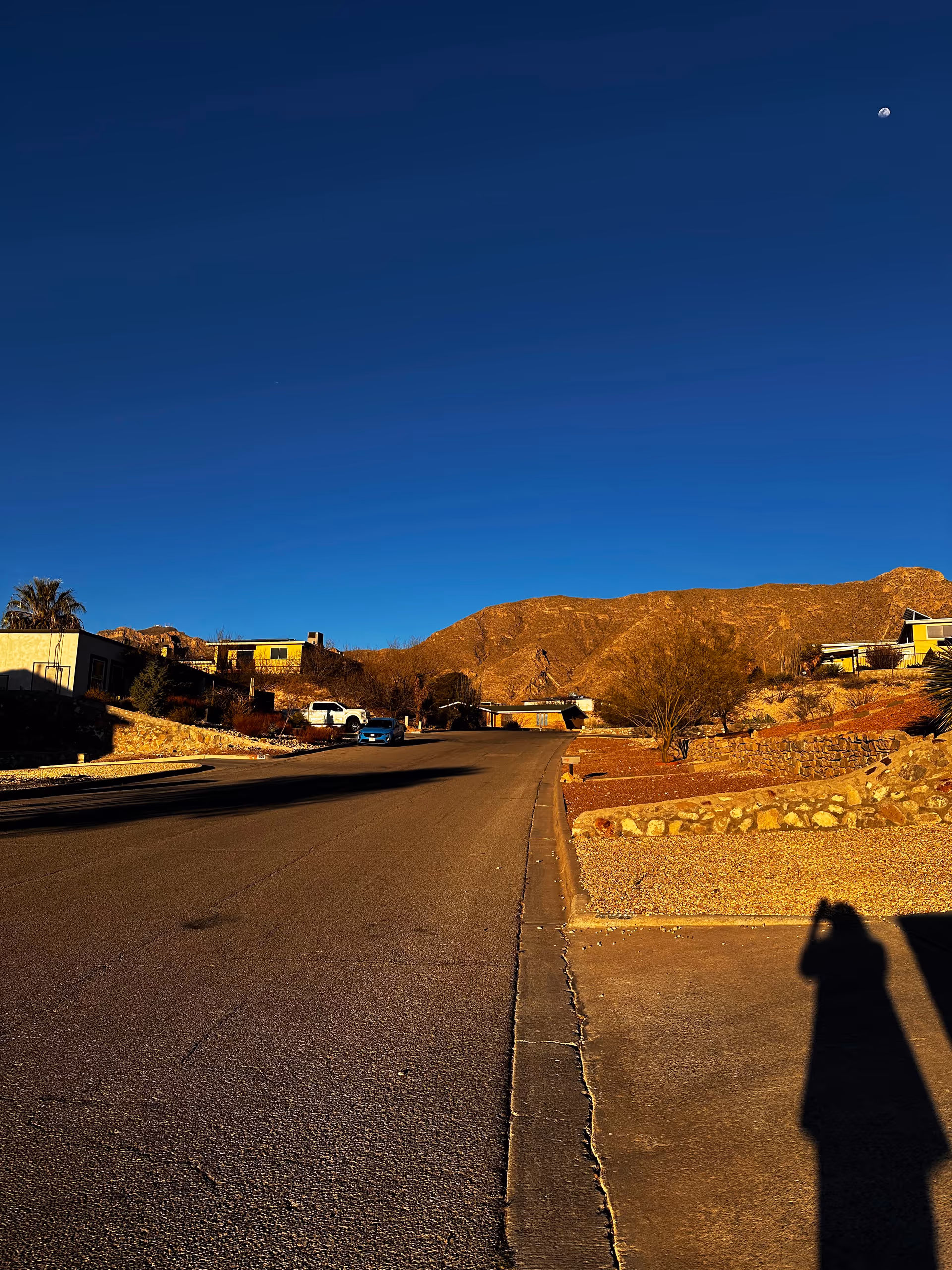 Desert suburban street with hills, modest houses, and a clear blue sky.