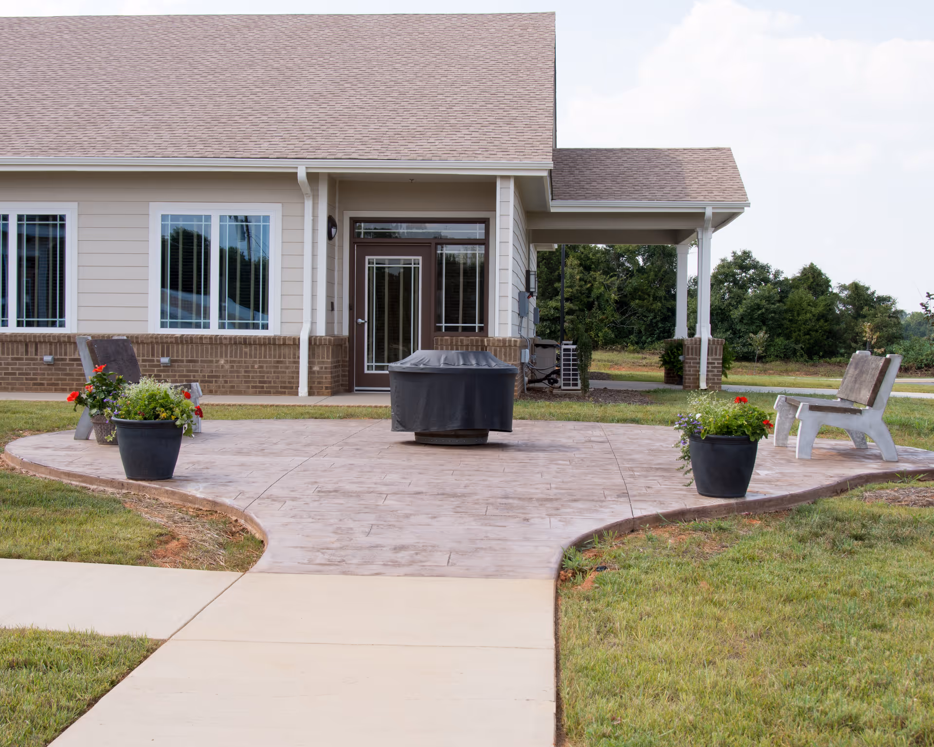 Curved patio with potted plants and a bench in front of a beige, single-story building.