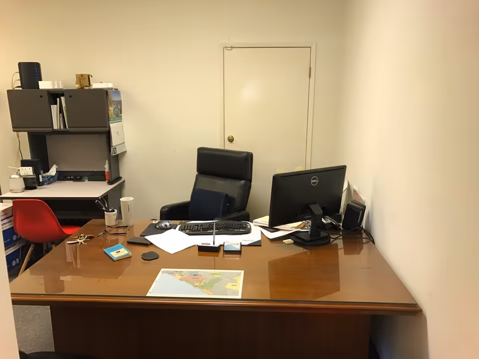 Office workspace with desk, computer, and filing shelves in a small room.