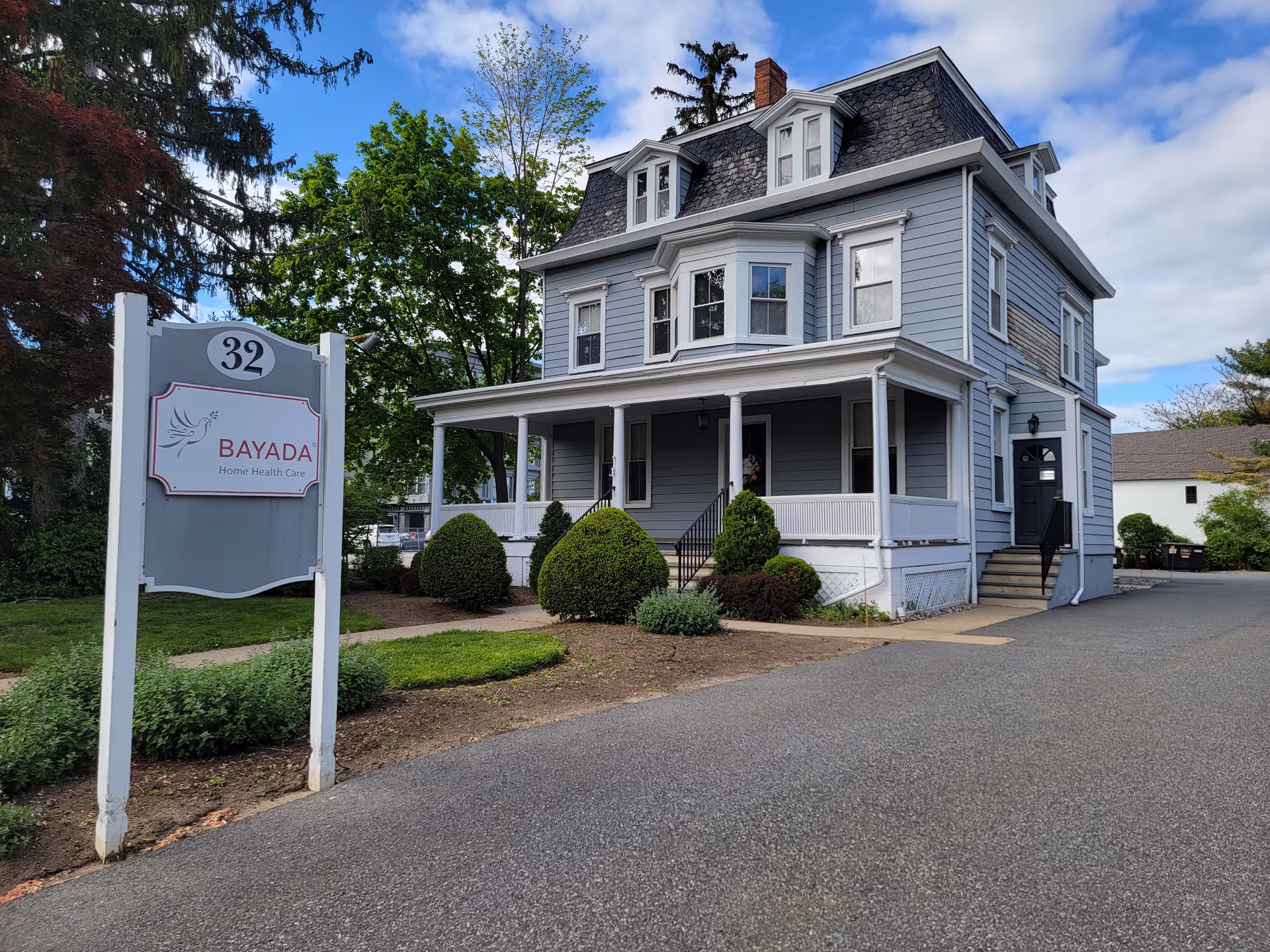 Blue-gray, two-story building resembling a house with a BAYADA sign and manicured shrubs.