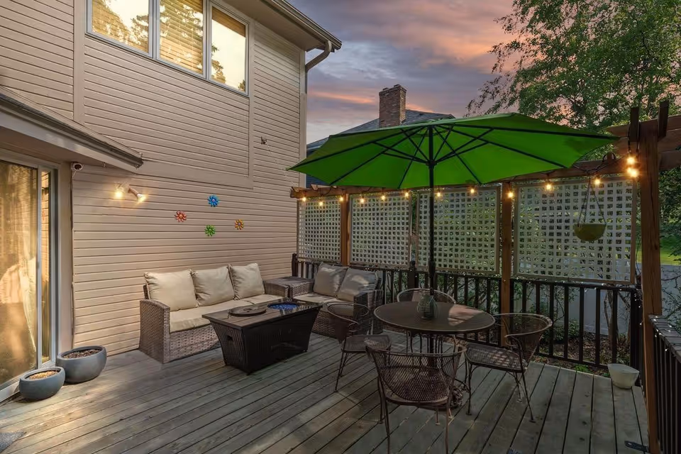 Outdoor patio with wicker seating, a round table, green umbrella, and string lights.