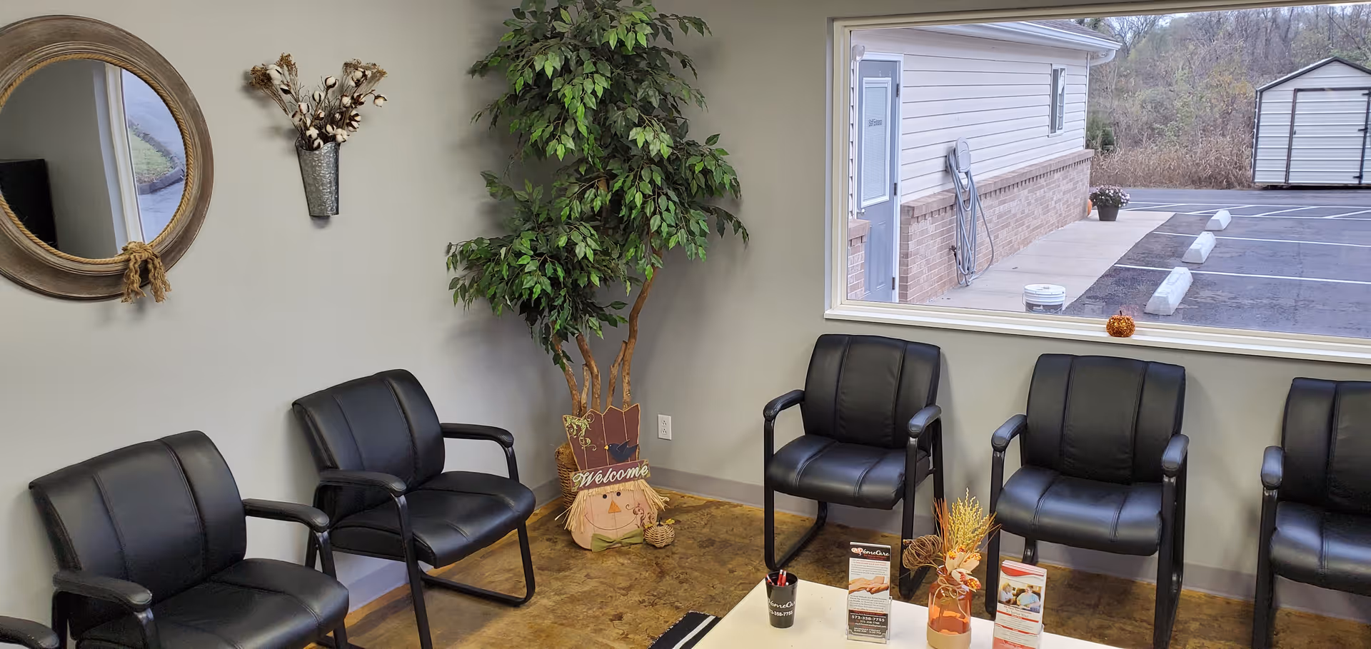 Lobby waiting area with black leather chairs, plants, and a window overlooking a parking lot.