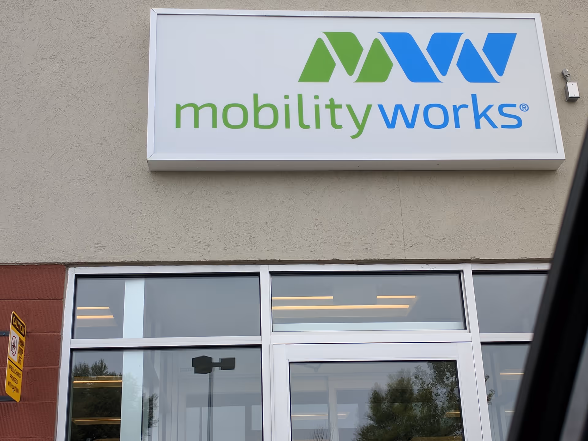 Exterior view of a MobilityWorks sign mounted on a beige building facade above glass doors.