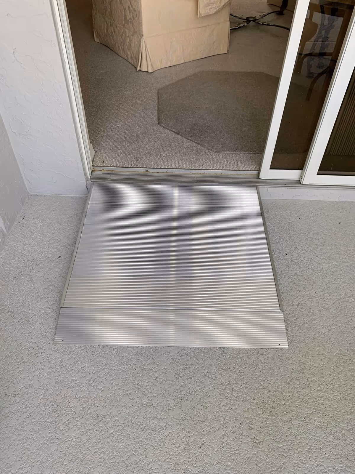 Sliding glass door opens to a carpeted interior with a metal ramp plate at threshold.