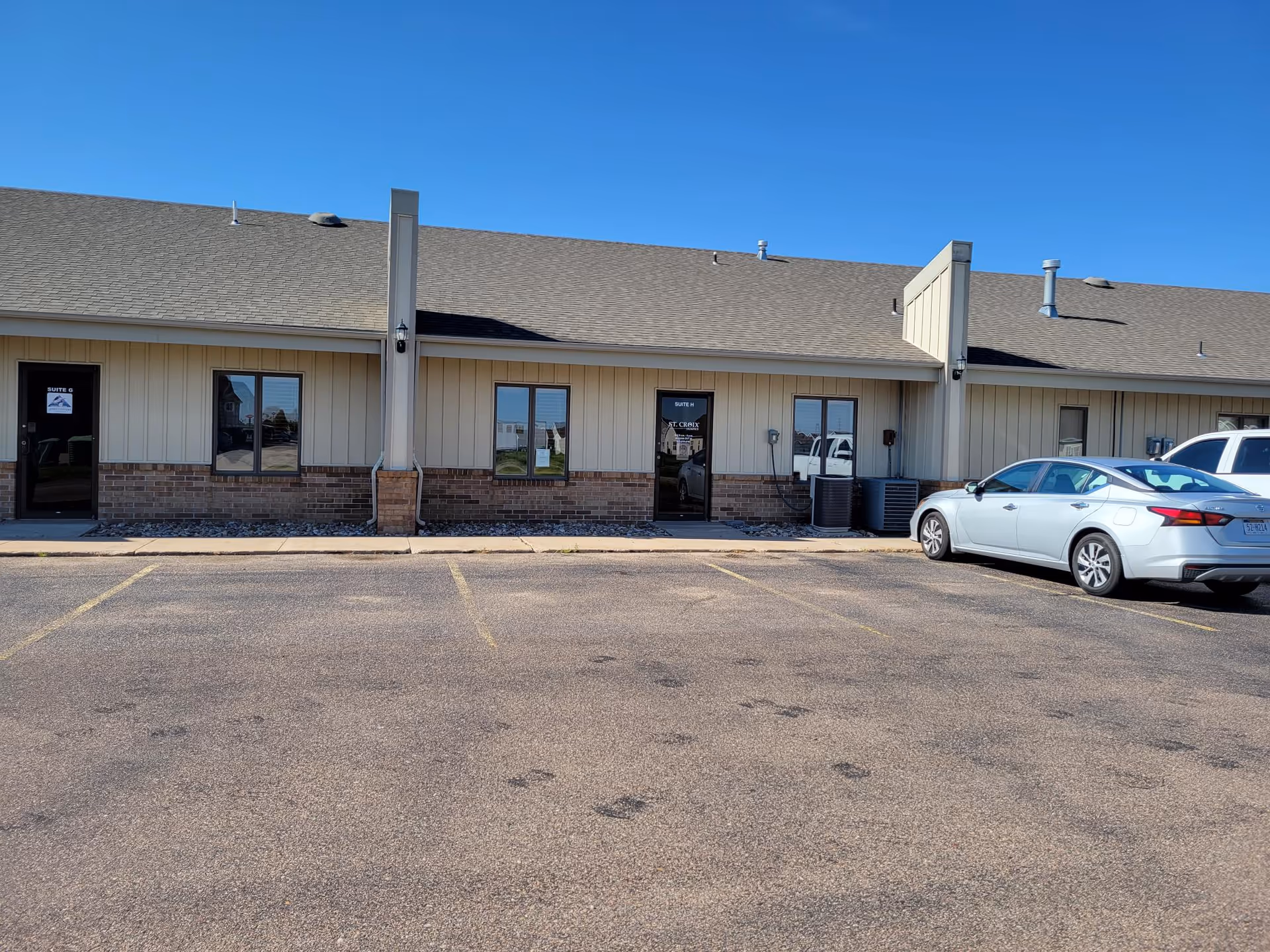 Front view of a single-story facility with beige siding, brick base, and parked cars.