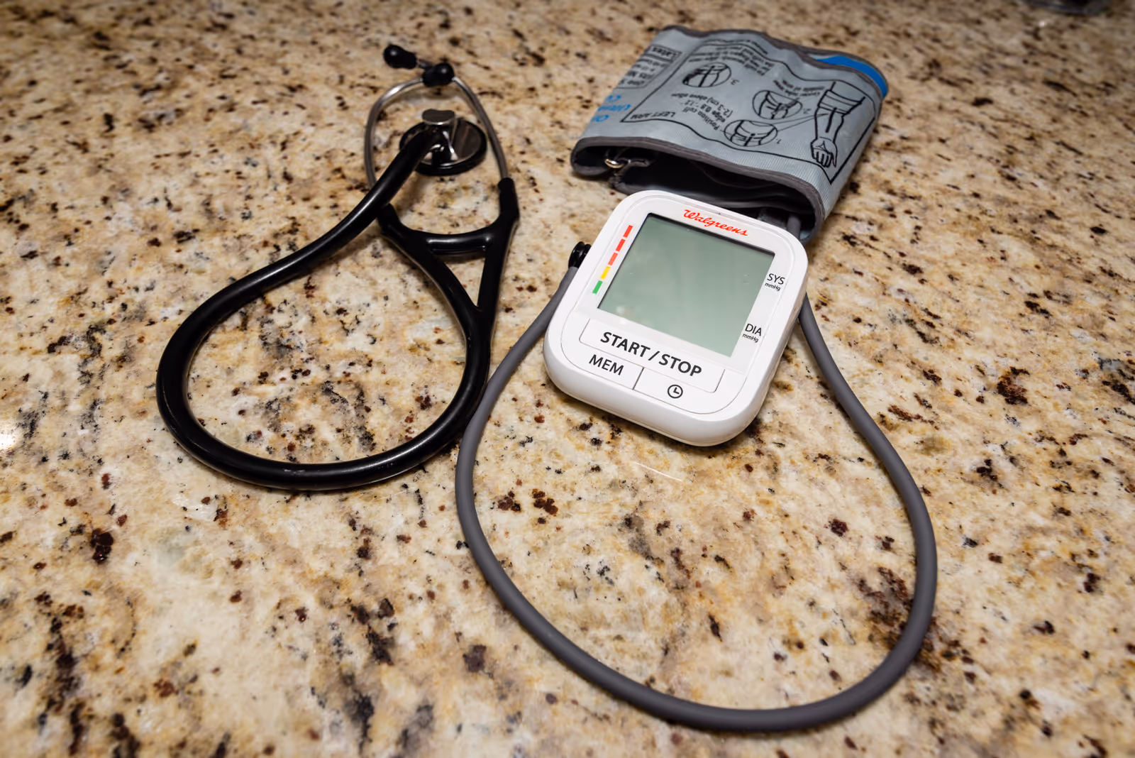 A digital blood pressure monitor with cuff sits on a speckled countertop.