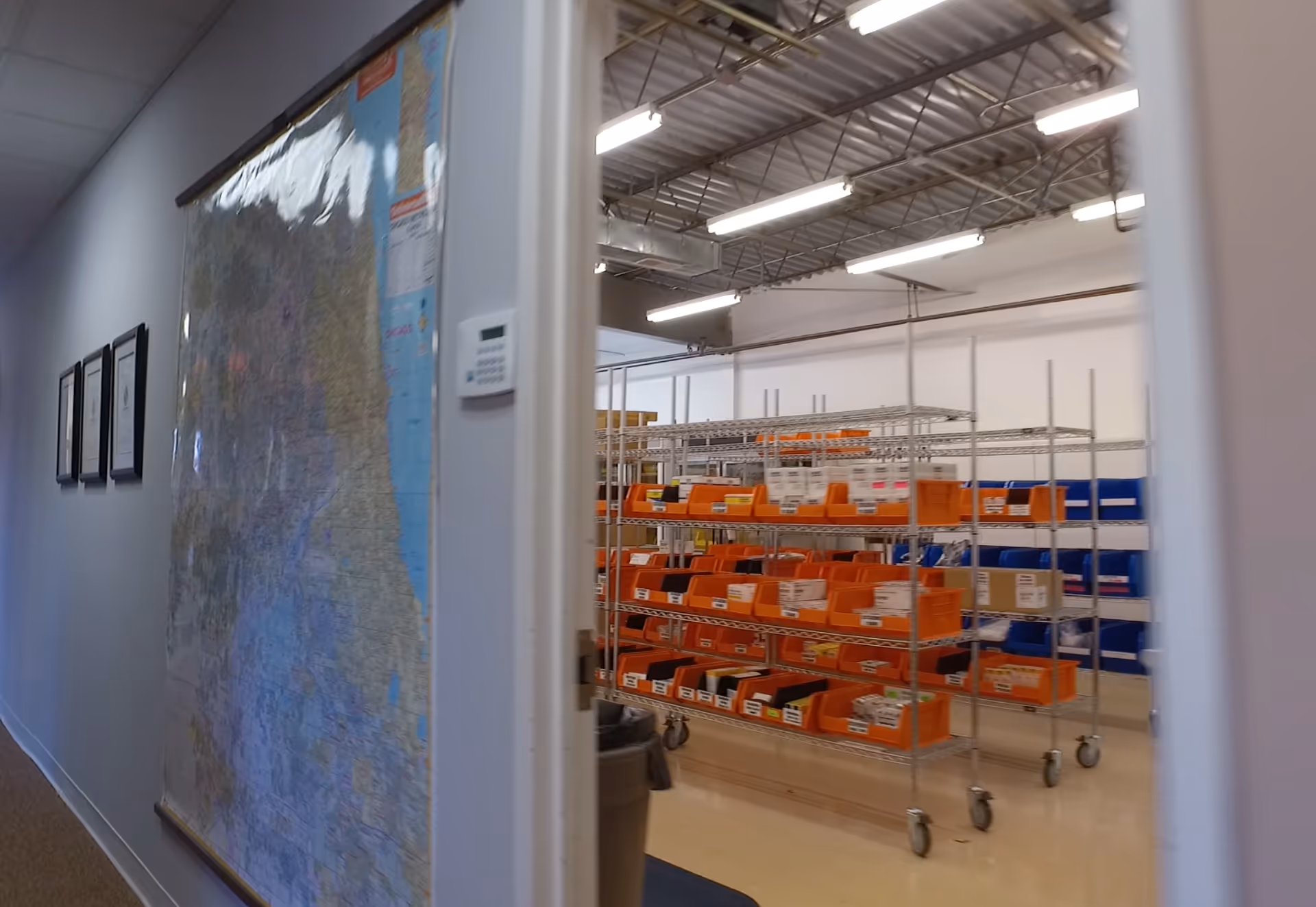 Indoor facility corridor with a large wall map and orange storage bins on shelves.