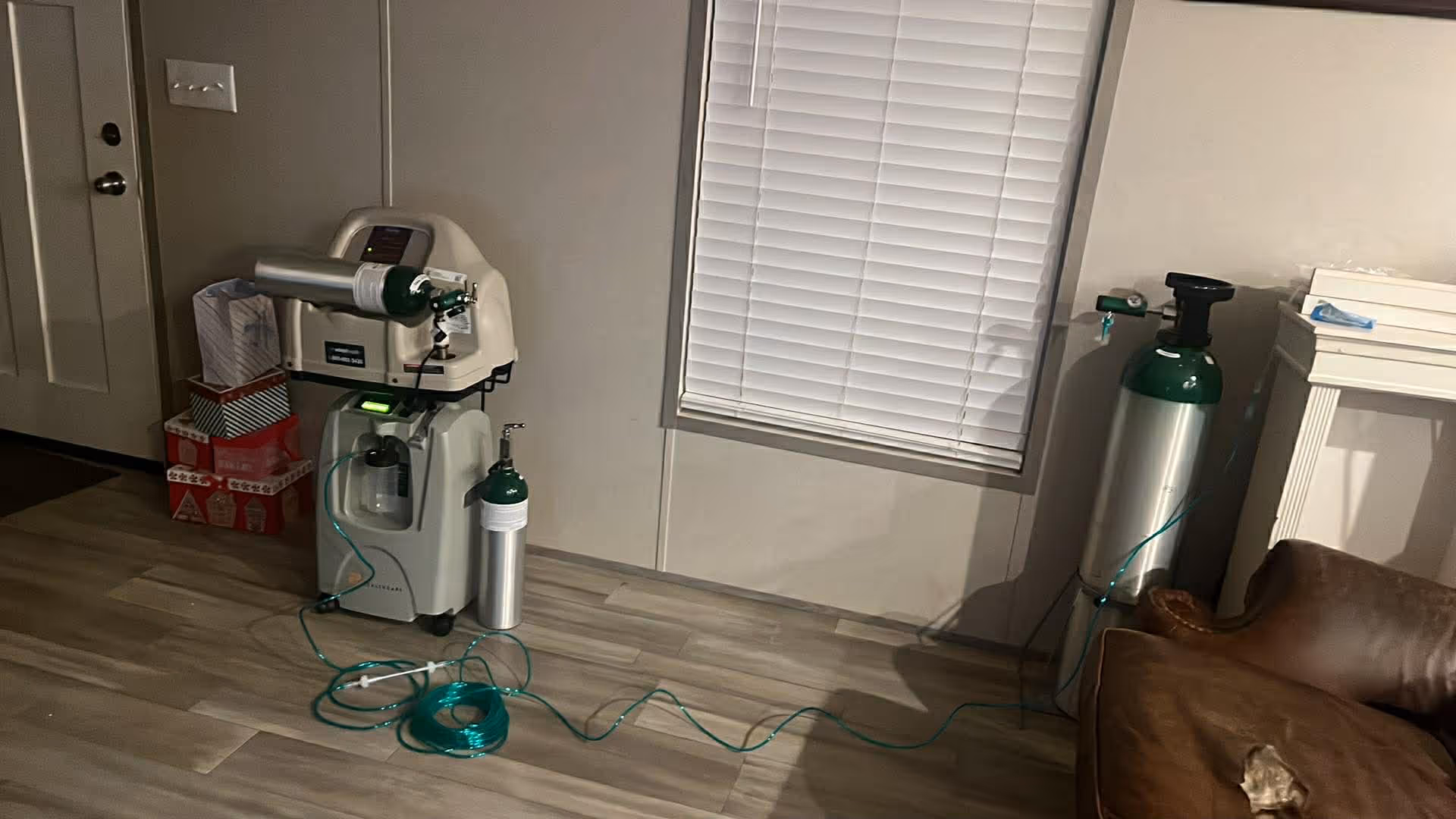 Interior living area with oxygen concentrator, cylinders, hoses, and a brown sofa.