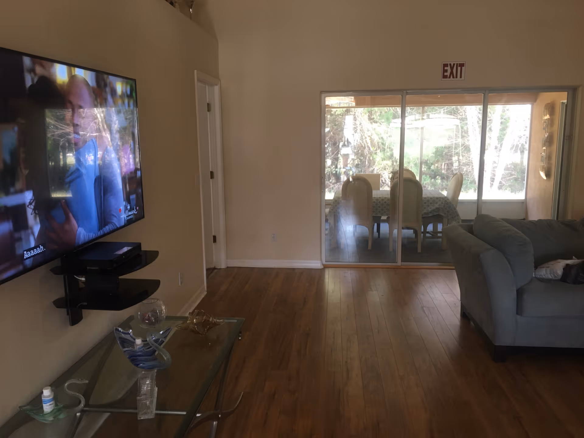 Living room with wall-mounted TV, glass coffee table, sofa, and sliding door to dining patio.