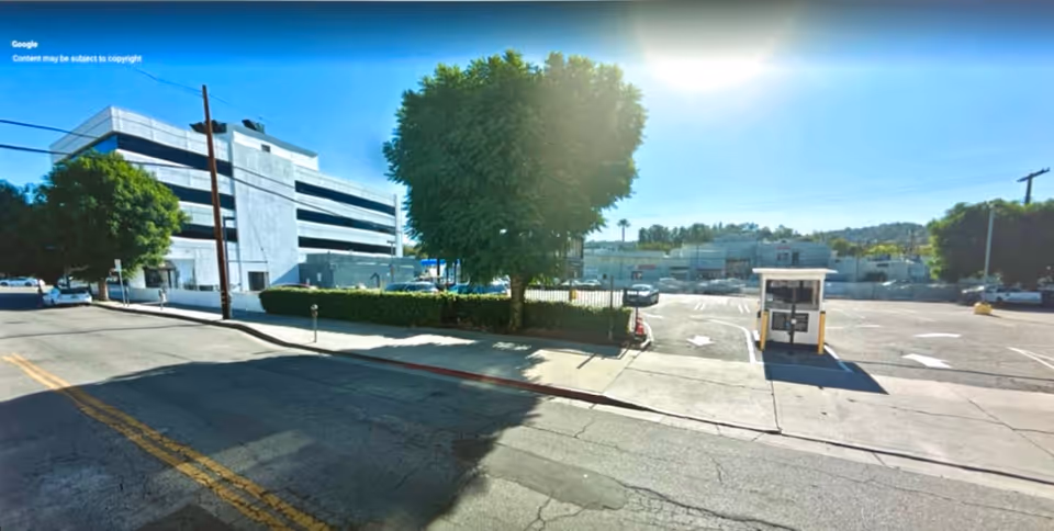 Exterior view of a facility with parking area, trees, and a small guard booth.