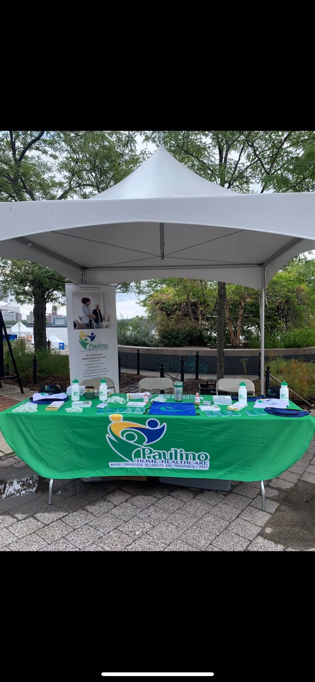 Outdoor booth with a green Paulino Home Healthcare table under a white canopy.